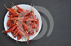 High angle of heap of red chilli peppers on the white plate isolated over black background
