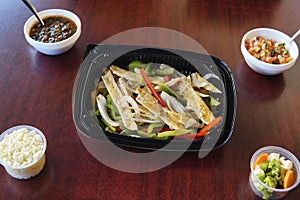 High angle of Mexican fajitas with sliced peppers accompanied rice, salsa and veggies