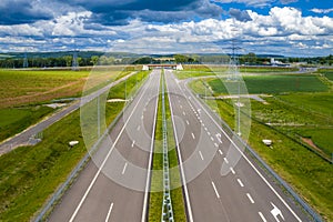 High angle panorama of straight asphalt highway passing through the mountain rural area at sun and clouds spring weather