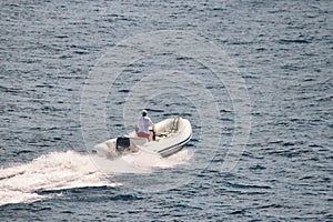 High-angle photo of an man driving a white rigid-hull inflatable boat in the water