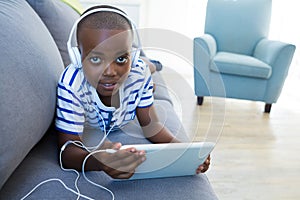 High angle portrait of boy using digital tablet while listening to headphones on sofa at home