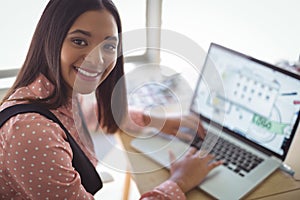 High angle portrait of smiling businesswoman working on laptop at office