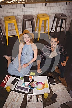 High angle portrait of smiling young creative professionals sitting on floor with sheets