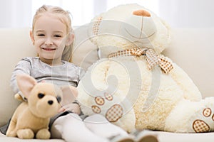 High angle portrait of a young smiling girl with stuffed toy sitting on sofa in the living room at home.