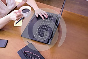 High angle shot of a busy businesswoman using her laptop working at home while drinking coffee