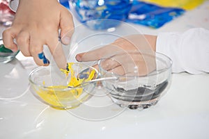 High angle shot of a child painting with his fingers with blue and yellow paint on a white table