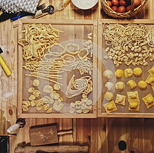 High angle shot of different shapes of macaroni and some ingredients on a wooden table