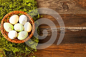 High angle shot of Easter eggs with painted flowers in a straw basket on a wooden table