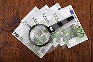 High angle shot of European money lying on the table under a magnifying glass