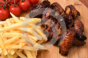 High angle shot of french fries on a wooden board with cherry tomatoes and roasted chicken on it