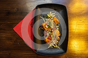 High angle shot of fried mozzarella sticks with lime and salad in a black plate on the table