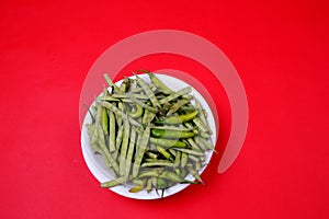 High angle shot of green beans and chili pepper on plate isolated on red background
