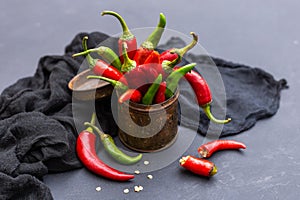 High angle shot of the green and red hot chili peppers in a rusty cup with cloth on a dark tabletop