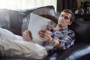 Surfing on his sofa. High angle shot of a handsome young man using his tablet while sitting on the sofa at home.