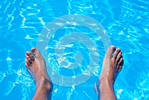 High angle shot of male feet in the bright blue water of a swimming pool