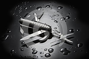 High angle shot of metal multi-purpose knife with water droplets isolated on black background