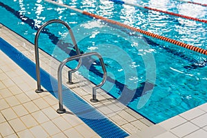 High angle shot of a metal swimming pool ladder with a pool lane in a background.