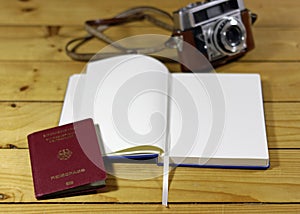 High angle shot of an open notebook next to a passport and a camera on a wooden surface