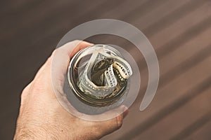 High angle shot of a person holding a jar of dollar bills over a wooden background