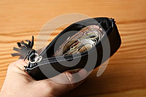 High angle shot of a person holding a leather wallet full of money over a wooden surface