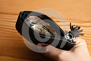 High angle shot of a person holding a leather wallet full of money over a wooden surface