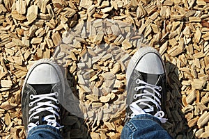 High angle shot of a person's feet standing on the ground covered with chops of wood