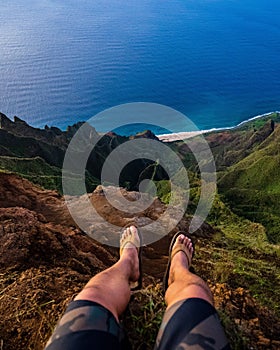 High angle shot of a person sitting on a cliff and looking down on the Napali Coast, Kauai, Hawaii