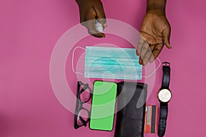 High angle shot of a person using hand sanitizer over a mask, phone, watch, wallet and glasses