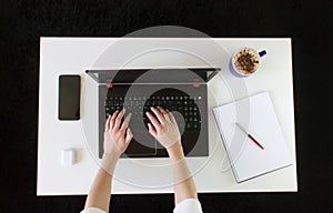 High angle shot of a person working at a work desk with a laptop, a cup of coffee, and mobile phone