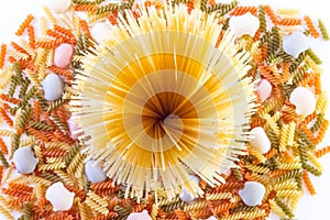 High angle shot of a pile of spaghetti on a lot of Italian colored pasta on a white surface