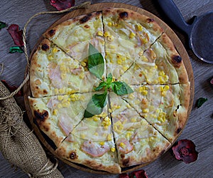 High angle shot of a pizza with ham and corn on a wooden tray