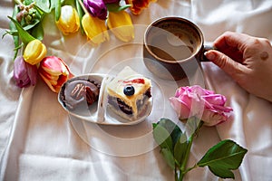 High angle shot of a plate with gourmet sweets and a cup of coffee on a white sheet with flowers