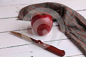 High angle shot of a red apple, a knife, and a checkered cloth on a white wooden surface