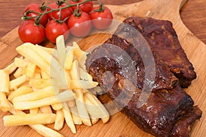 High angle shot of roasted meat on a wooden board with french fries and cherry tomatoes on it