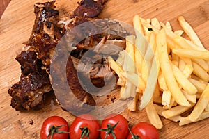 High angle shot of roasted meat on a wooden board with french fries and tomatoes on it