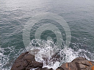 High angle shot of a sea crashing on the shore cliffs with waves
