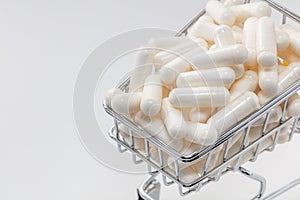 High angle shot of a small shopping cart full of white pills. White background, copy space. Close up shot. Shopping online, buying