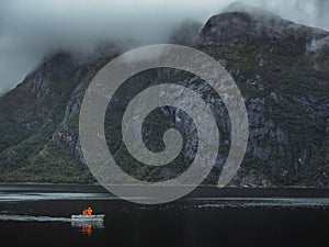 High angle shot of two fishermen in the boat in the lake beside the foggy mountains