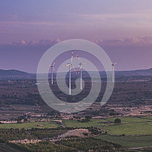 High angle shot of wind turbines near the green farms under the cloudy sky