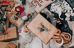 High angle shot of a woman holding a brown gift box lying down on the carpet