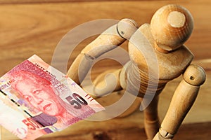 High angle shot of a wooden figure and a fifty rand bill on a wooden surface