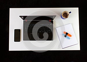 High angle shot of a work desk with a laptop, a cup of coffee, mobile phone, notepad, and headphones