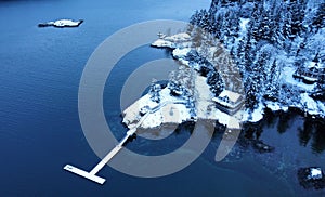 High angle of a snowy shore with houses and a dock.with water and a small island in the background