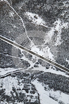 High angle top down aerial view drone image on road trough the trees and forest in mountain range covered with white snow in