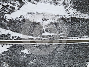 High angle top down aerial view drone image on road trough the trees and forest in mountain range covered with white snow in