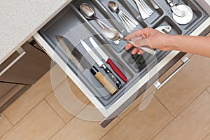 High angle top view cropped photo of woman hand open kitchen drawer by modern door handle, with different cutlery and take spoon