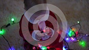 High angle view absorbed curios baby playing with Christmas light in slow motion sitting on soft carpet at home indoors