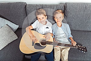 high angle view of adorable little brothers with guitar smiling at camera while sitting on sofa