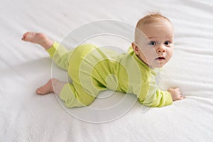 High-angle view of adorable newborn baby girl wearing yellow cotton bodysuit lying on stomach on white sheet. Newborn