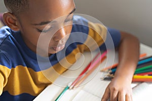 High angle view of african american elementary schoolboy drawing on book at desk in classroom